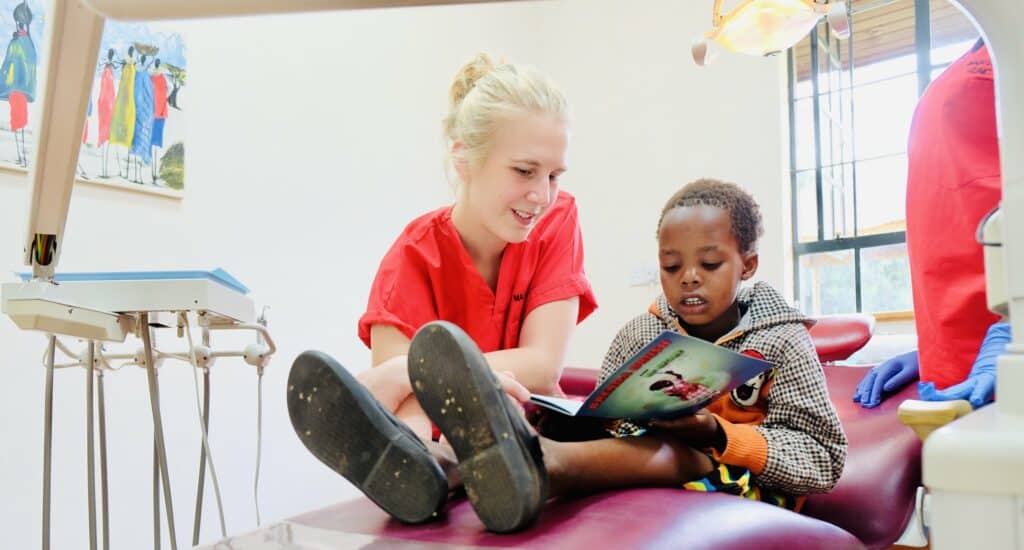 A dental assistant reading a book with a young boy.